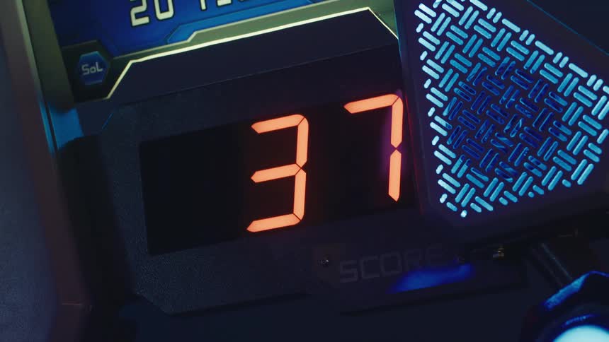 A close-up of a futuristic arcade game's digital scoreboard as the score increases from 34 to 38