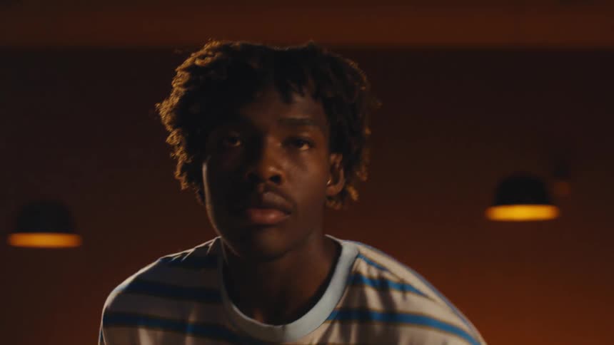 A young Black man reveals his face from behind a green bowling ball and closes his eyes with intense concentration