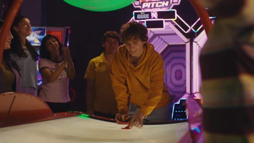 Two young men face off in an exciting game of air hockey as their friends watch and cheer in a vibrant arcade
