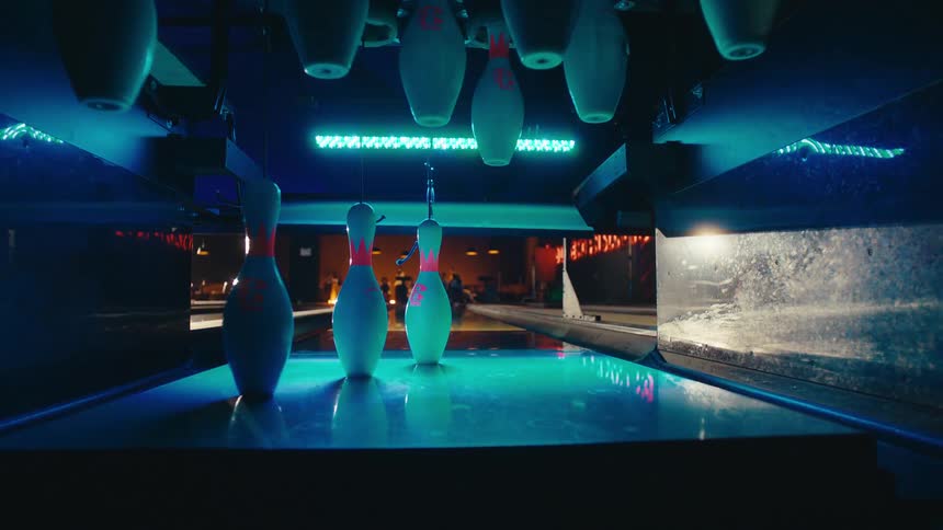 A bowling ball rolls down the lane and strikes the pins in a dramatic point-of-view shot from behind the pins