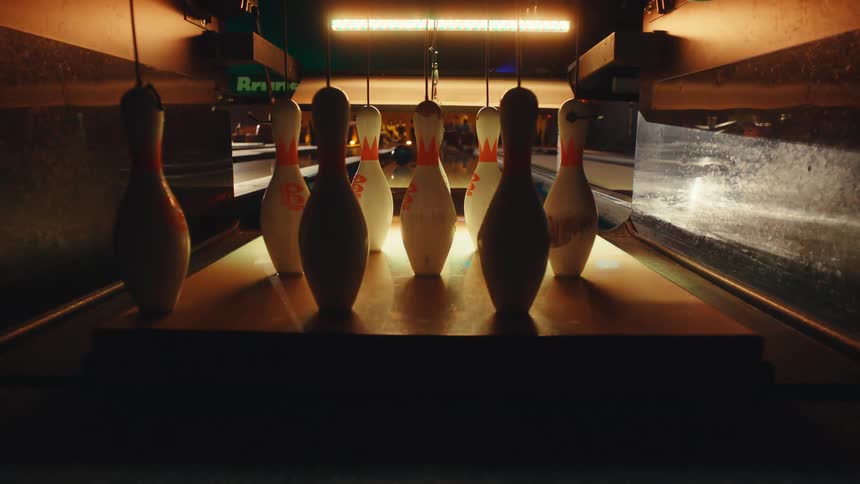 A close-up, slow-motion shot from the end of the lane as a bowling ball strikes the pins under colorful lights