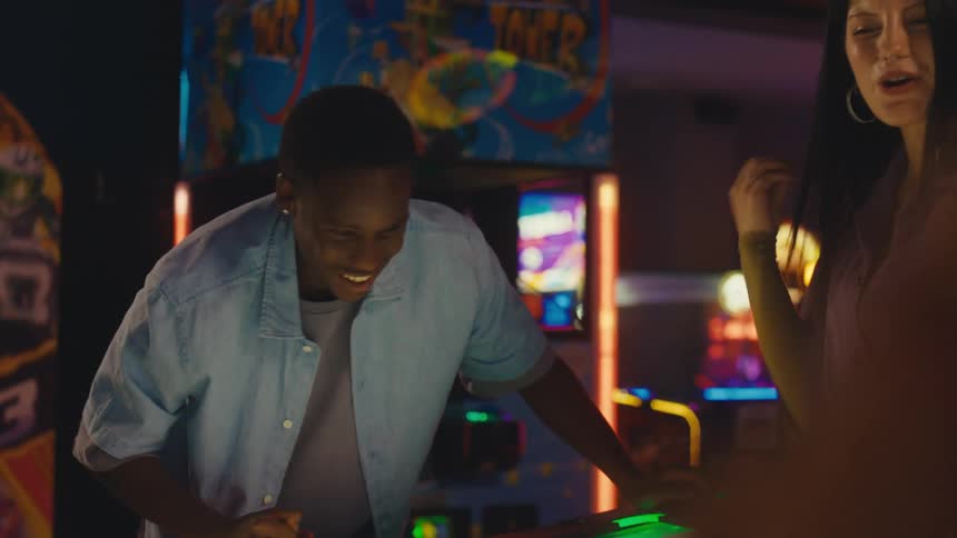 A group of diverse friends have a fun and competitive game of air hockey in a brightly lit arcade