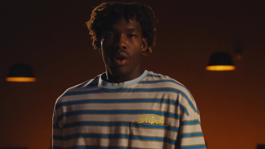 A focused young Black man reveals his face from behind a bowling ball before preparing to throw at an alley