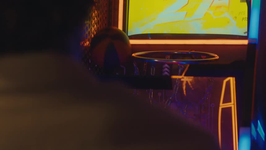 Slow-motion over-the-shoulder view of a person shooting hoops on a colorful neon arcade basketball game