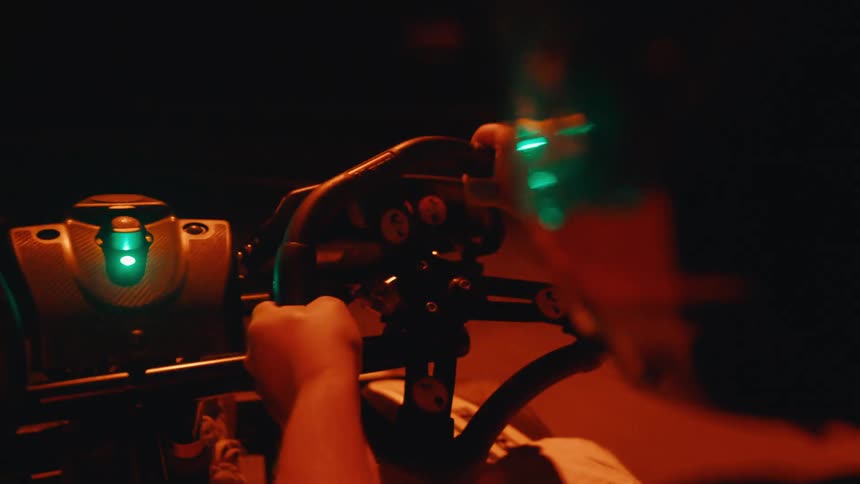 A first-person view of a go-kart race on a dark indoor track illuminated by intense red and green lights