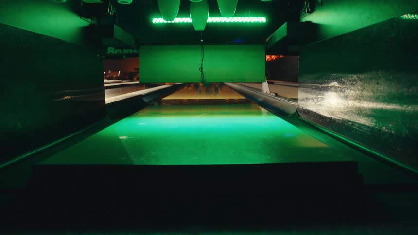 Close-up of an automatic pinsetter resetting bowling pins on a lane illuminated by green lights