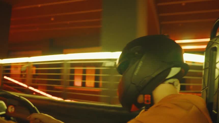 A man in a helmet drives a go-kart on a professional indoor race track with flashing neon lights