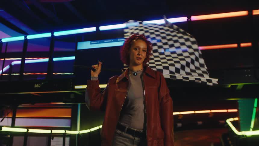A confident woman waves a checkered flag in slow motion at a neon-lit go-kart track