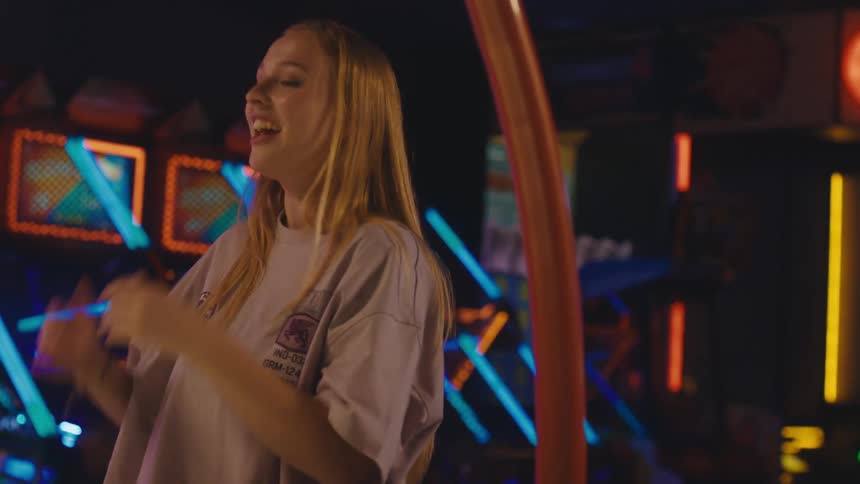 An ecstatic young woman laughs and dances while playing games with friends at a vibrant arcade