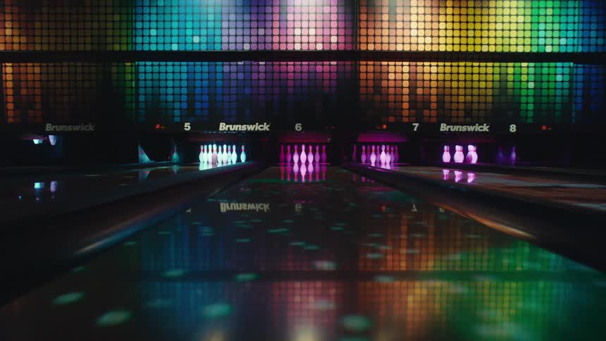 A slow, immersive camera push down a modern bowling lane, surrounded by a vibrant, colorful display of pulsing LED and disco lights