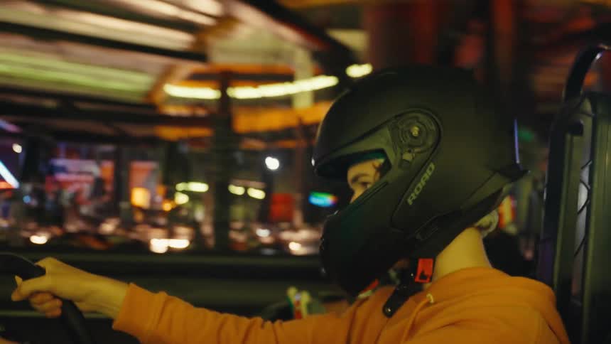 Close-up of a person wearing a helmet while driving a go-kart on a neon-lit indoor track