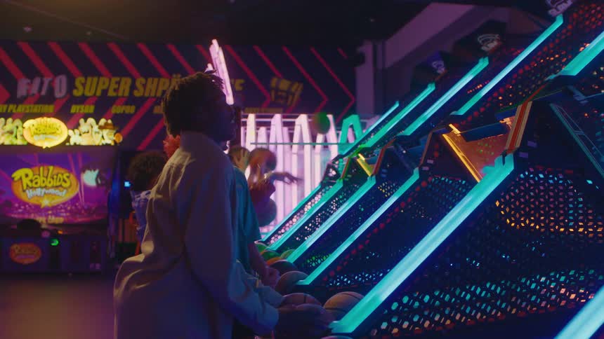 Friends have a fun and competitive time playing a classic basketball shooting game together at a neon-lit arcade