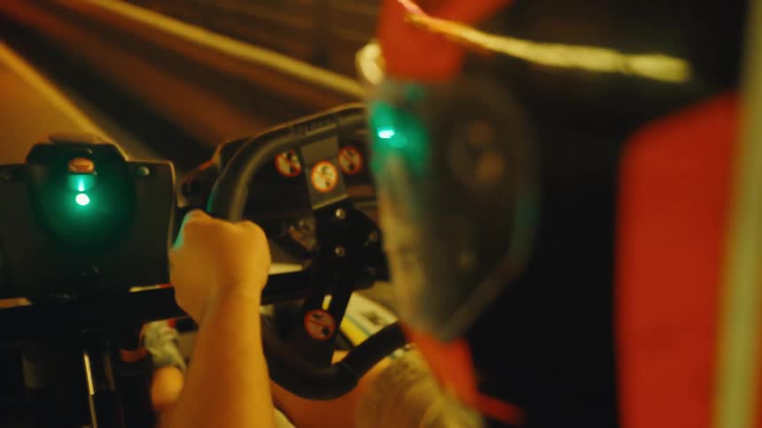 Over-the-shoulder slow motion view of a racer driving a go-kart on a neon-lit indoor track
