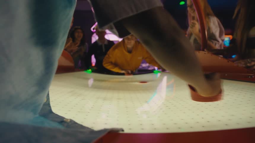 A group of friends cheer as a young man scores a point in a competitive game of air hockey at a neon-lit arcade