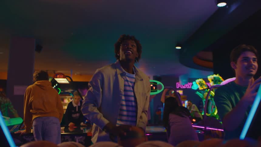 Two male friends have fun playing a competitive basketball arcade game in a neon-lit arcade