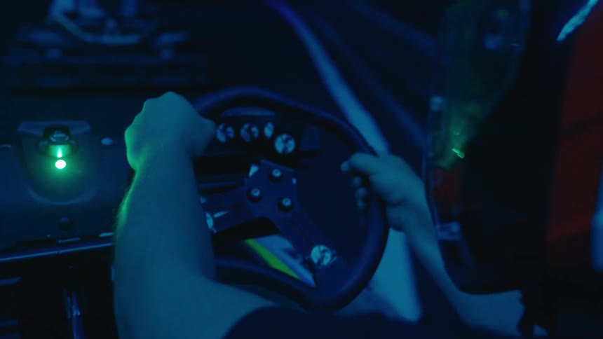 An over-the-shoulder view of a person racing a go-kart on a dark, neon-lit indoor track