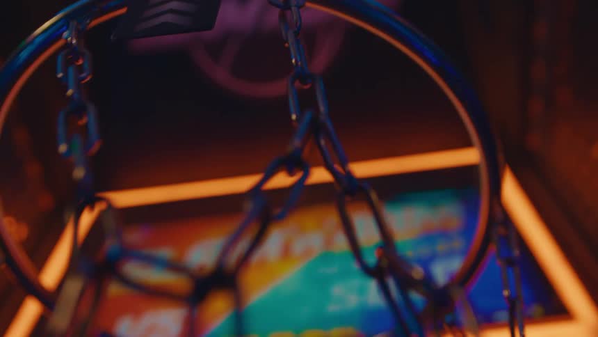 Slow motion close up of a basketball swishing through a neon-lit arcade game hoop