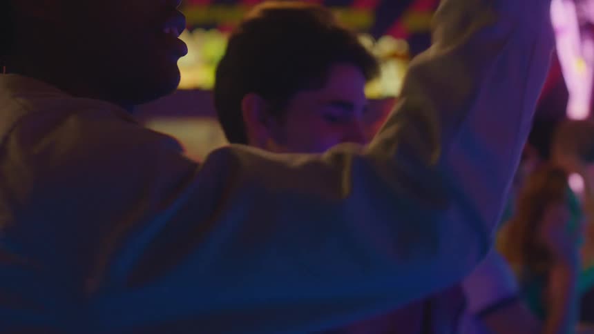 A diverse group of friends energetically play a basketball shooting game in a vibrant, neon-lit arcade