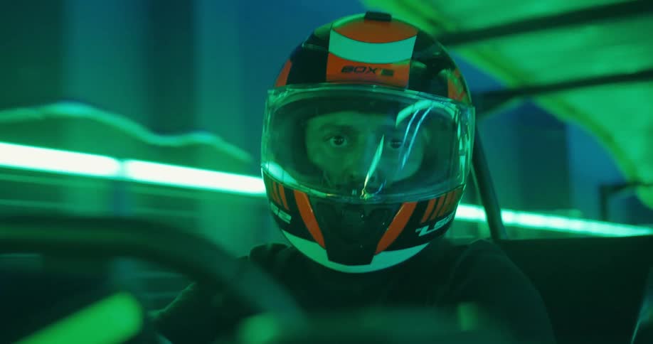 Intense close-up of a male driver in a racing helmet navigating a go-kart on a track with green neon lights