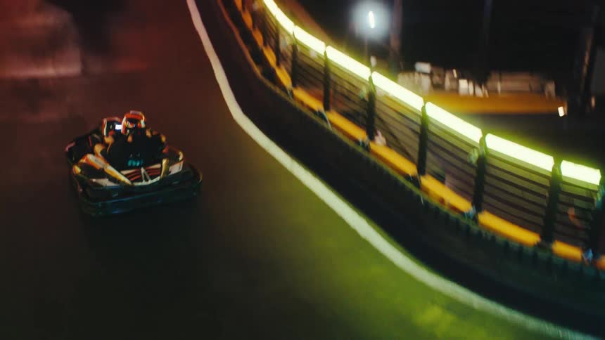 Go-karts race around a winding, multi-level indoor track illuminated by vibrant neon lights