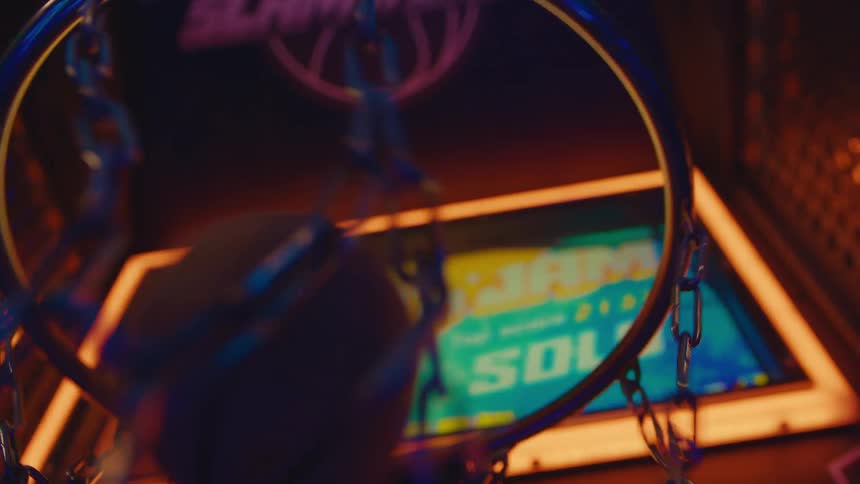 A basketball repeatedly goes through the chain net of a brightly lit arcade basketball game in slow motion