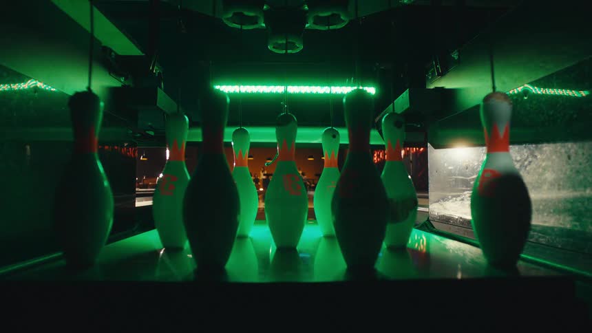 Close-up perspective of bowling pins standing at the end of a lane as the surrounding lights cycle through a vibrant spectrum of colors