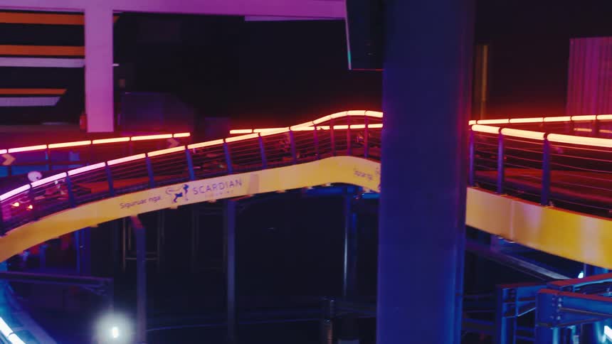 Go-kart racers speed around a futuristic, multi-level indoor track with colorful neon lights