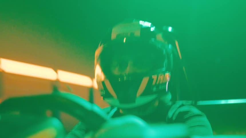 Intense close-up of a man in a racing helmet driving a go-kart through a dark, neon-lit tunnel
