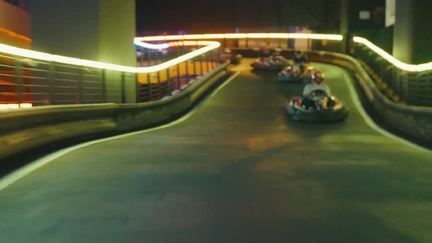 A thrilling first-person perspective of a go-kart race on a multi-level indoor track illuminated by colorful neon lights