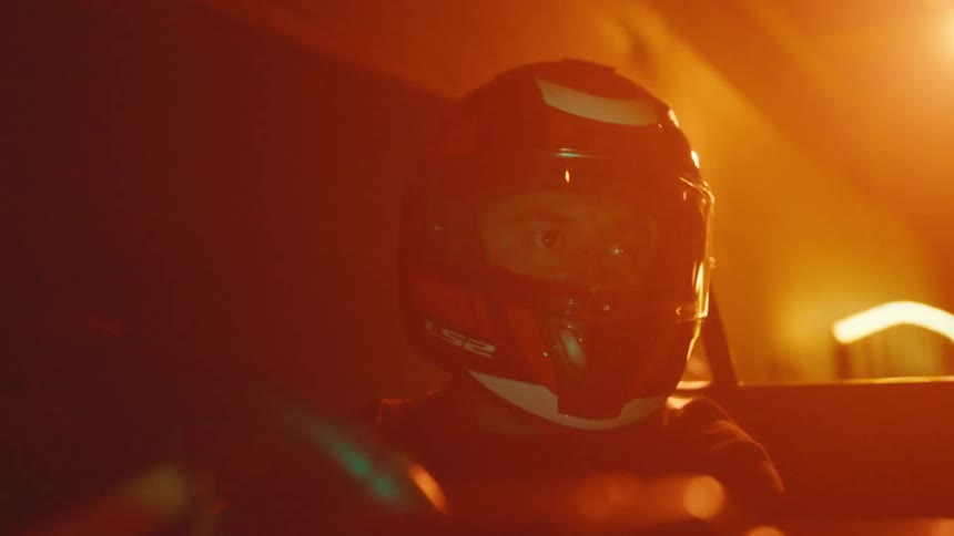 Close-up of a racer's intense gaze through his helmet visor as he speeds around a brightly lit indoor go-kart track