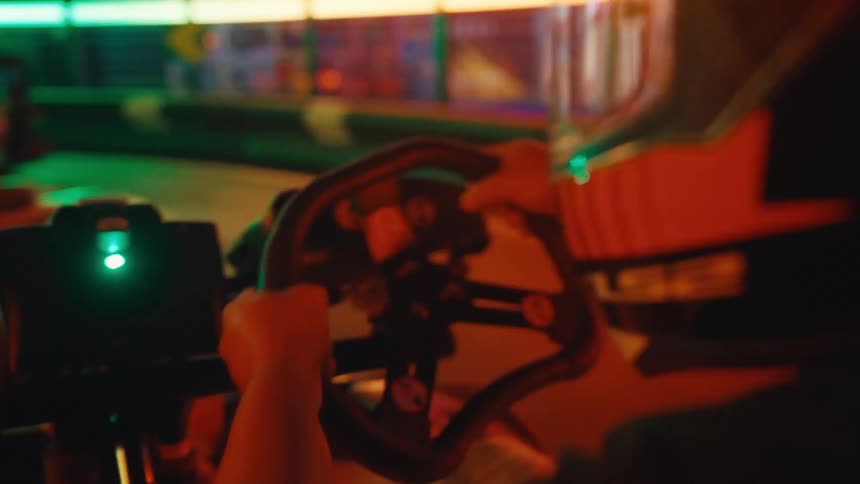 An over-the-shoulder view of a person racing a go-kart on a vibrant, neon-lit indoor track