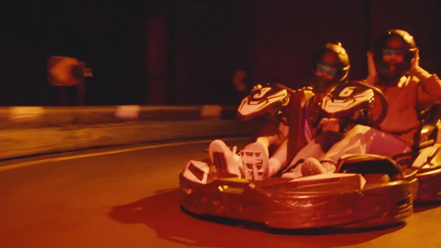 Friends have fun driving a go-kart on a futuristic neon-lit indoor race track