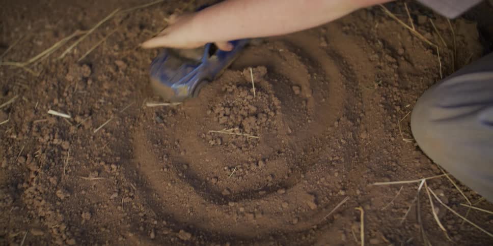 Overhead view of a boy in a cowboy hat playing with a blue toy truck in the dirt, creating circular patterns