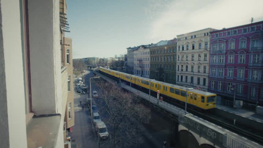 An iconic yellow Berlin subway train glides along an elevated railway past colorful urban buildings