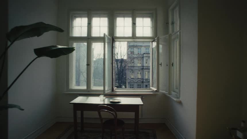 A slow zoom out reveals a view of a city train station from an open apartment window on a sunny day