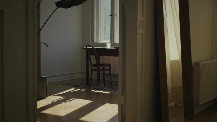 Sunlight streams into a quiet, empty room with a table and chair, revealed by a slow, cinematic camera pan