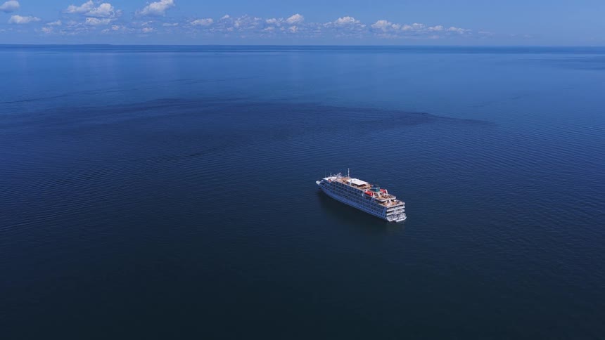 An aerial high-angle view of a large white cruise ship sailing on the calm deep blue ocean on a sunny day