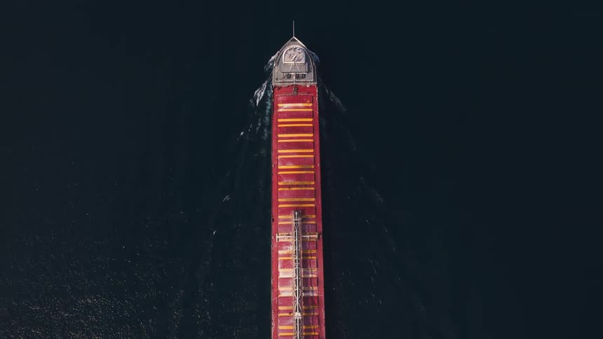 Birds-eye view of a massive red freighter ship navigating through the deep blue sea