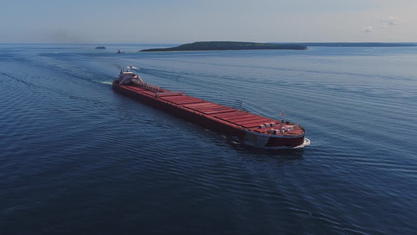 High aerial view of a massive red freighter ship cruising through the deep blue waters of a lake on a clear day