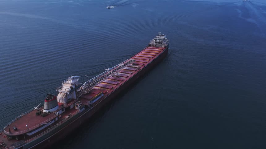 Impressive aerial view follows a massive cargo freighter sailing across the deep blue open water on a clear day
