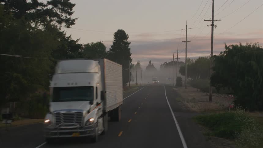 Aerial view moving down a foggy country road at sunrise as a semi-truck and other vehicles drive past