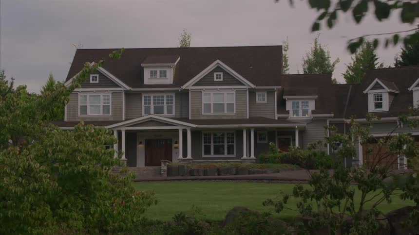 A slow pan reveals the exterior of a large, upscale suburban home on an overcast day