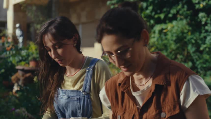 A young woman affectionately hugs her mother while they work together in their sunny backyard garden