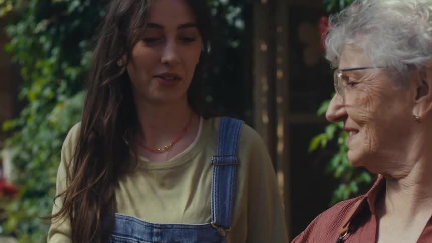 A loving granddaughter embraces her smiling grandmother from behind as they spend quality time gardening together in their sunny backyard