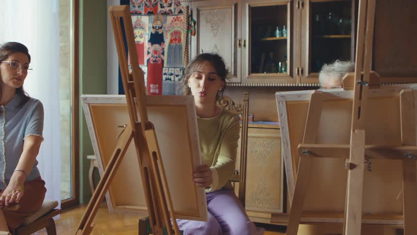 An art teacher instructs two female students of different generations during a cozy painting class at home