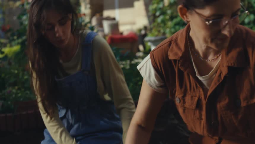 A mother and her daughter share a heartfelt moment, talking and hugging while planting flowers in their lush garden