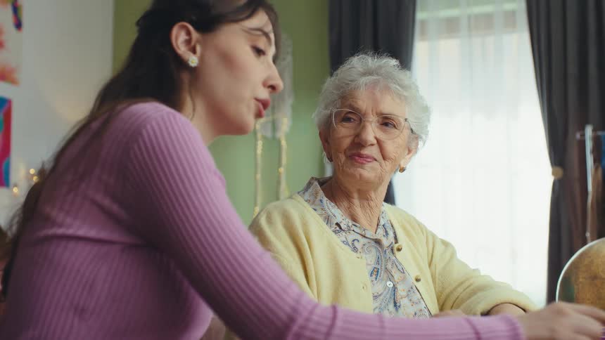 A slow motion shot shows a young woman teaching her elderly grandmother how to use a laptop