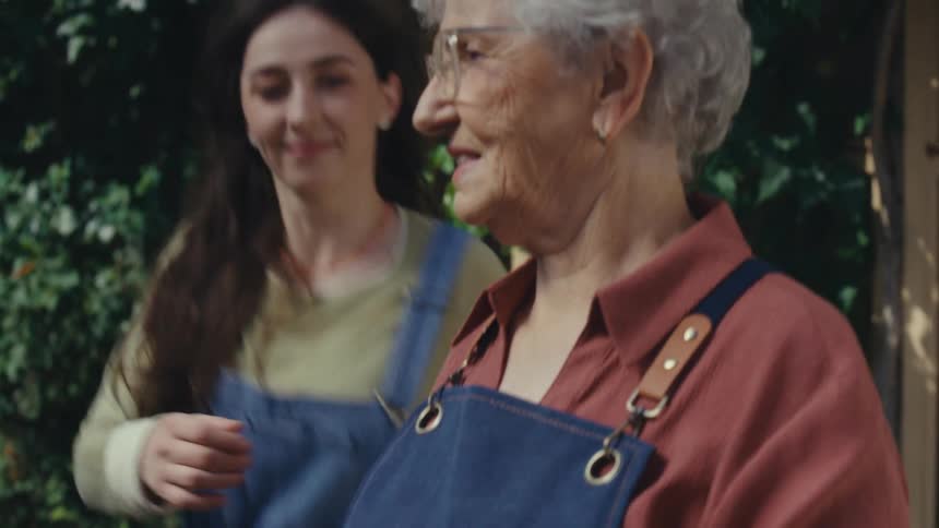 A loving granddaughter surprises her grandmother with a warm hug while she tends to her flower garden