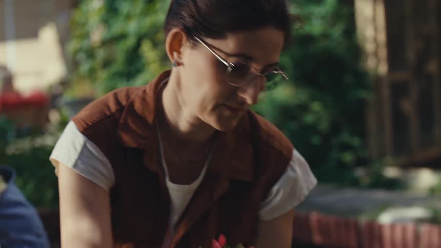 A close-up slow-motion shot reveals a mother and daughter bonding while planting vibrant flowers in their sunlit garden