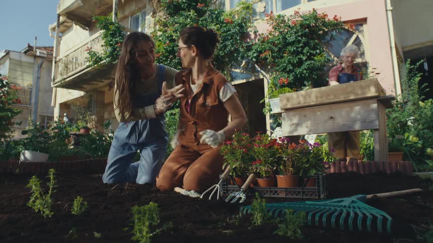 Three generations of women share a beautiful moment gardening together in their lush backyard, as a mother teaches her daughter how to plant flowers with grandma looking on
